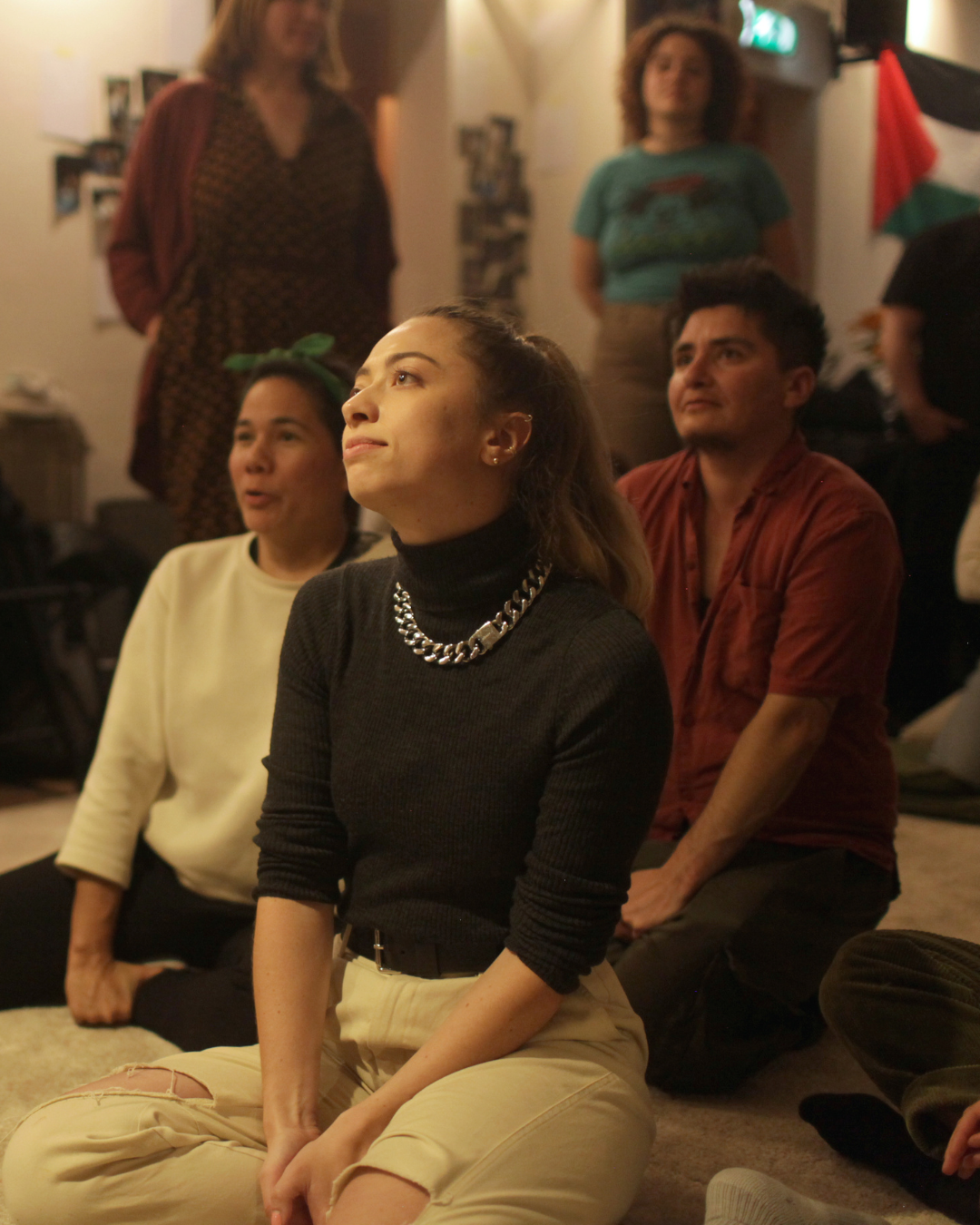 Three people sit together on the ground while paying attention to the instructor of the workshop